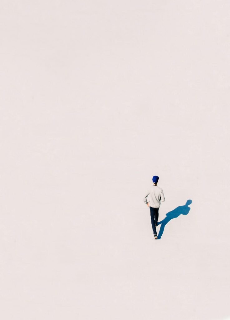 A single person walking in a minimalist setting casting a distinct shadow.