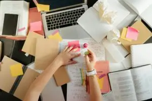 A cluttered desk with notebooks, sticky notes, and a laptop, depicting a student's busy life.